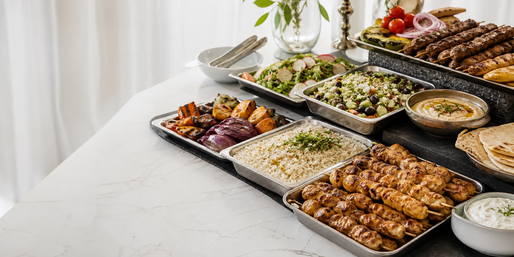 Mediterranean catering trays with grilled meats, rice, salads, pita, and sauces.